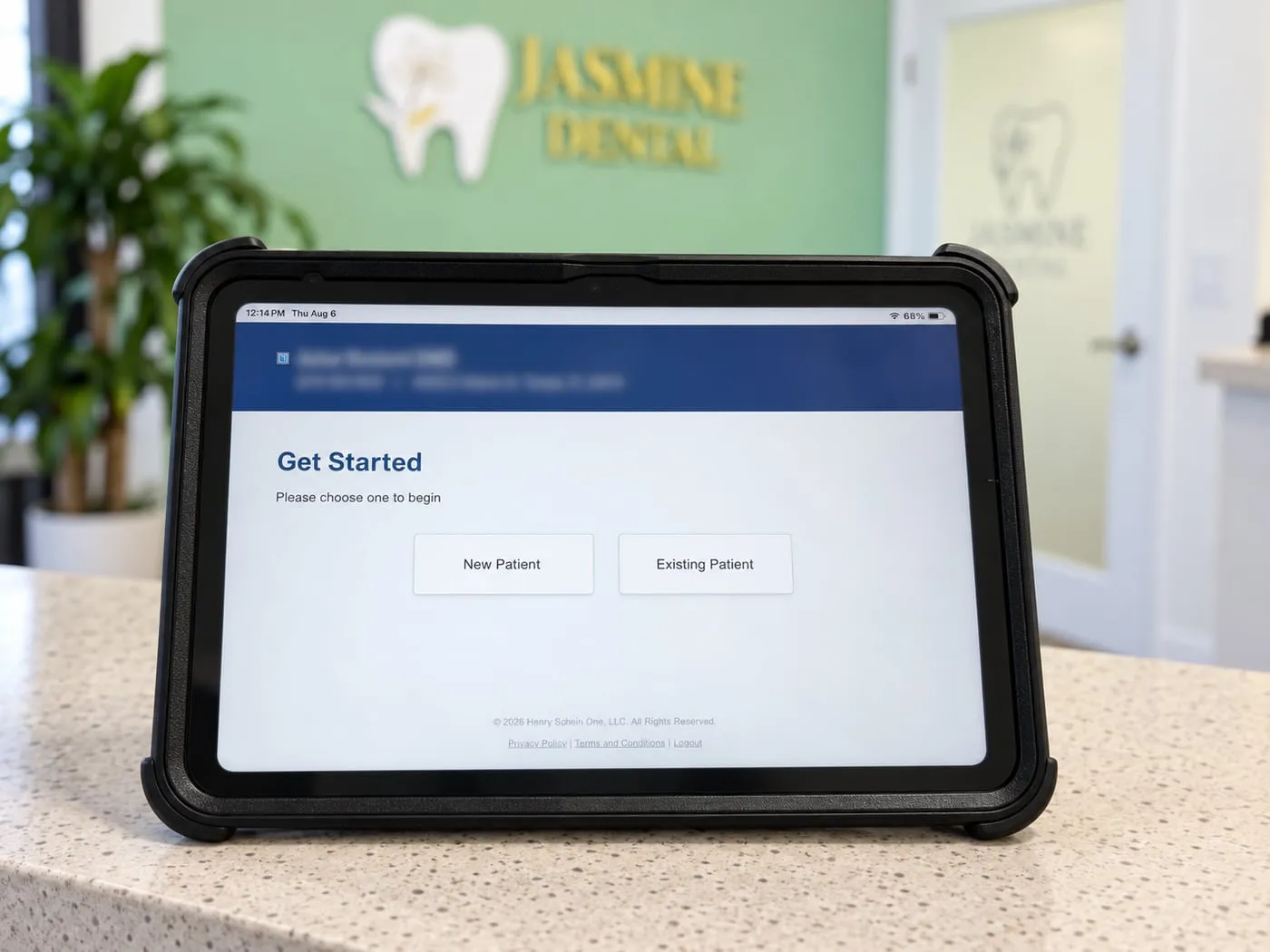 An iPad on the front desk counter at Jasmine Dental showing the patient check-in screen, headed Get Started with New Patient and Existing Patient buttons. The practice's tooth logo is on the wall behind it.