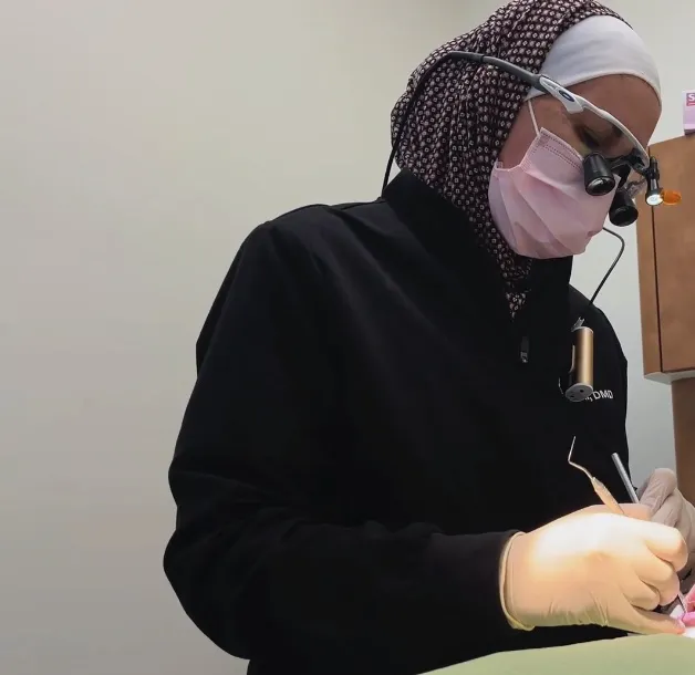 Dr. Bustami working chairside on a patient, wearing surgical loupes and a
mask, in a treatment room at Jasmine
Dental.