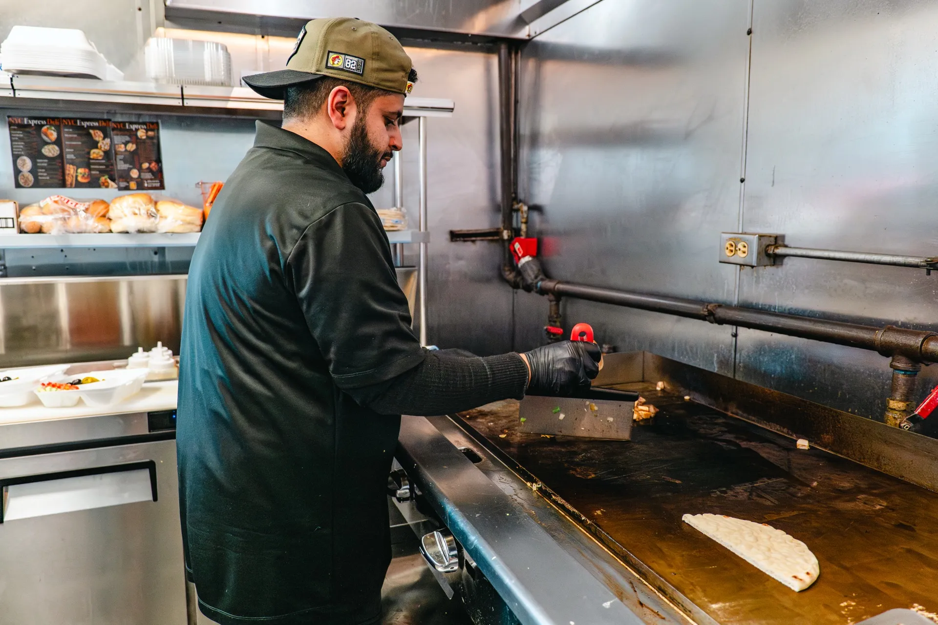 The owner of NYC Express Deli working the griddle in the Rogers kitchen, menu boards on the wall behind him.